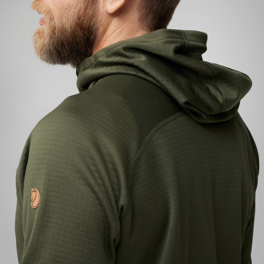 Person wearing a green hooded jacket with a brand logo on a gray background