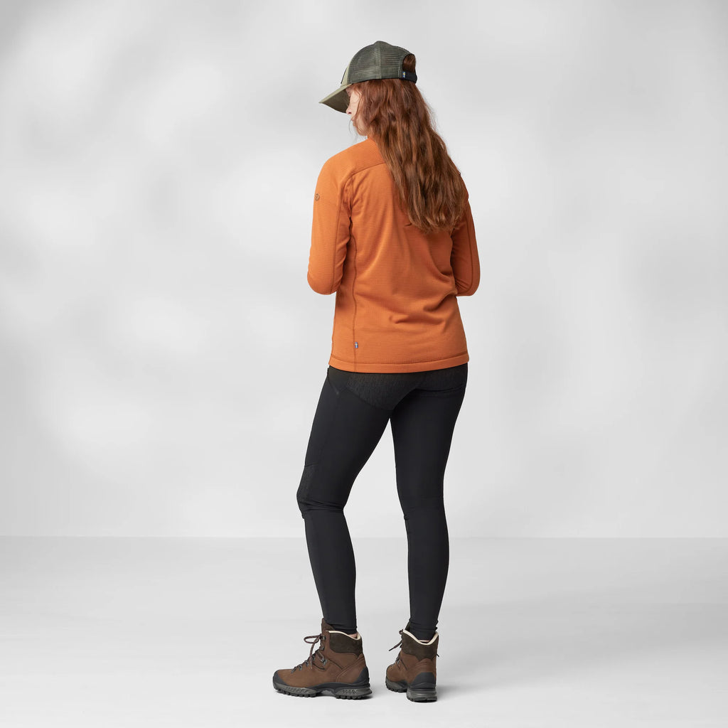 Person wearing an orange fleece, black leggings, and brown boots on a white background