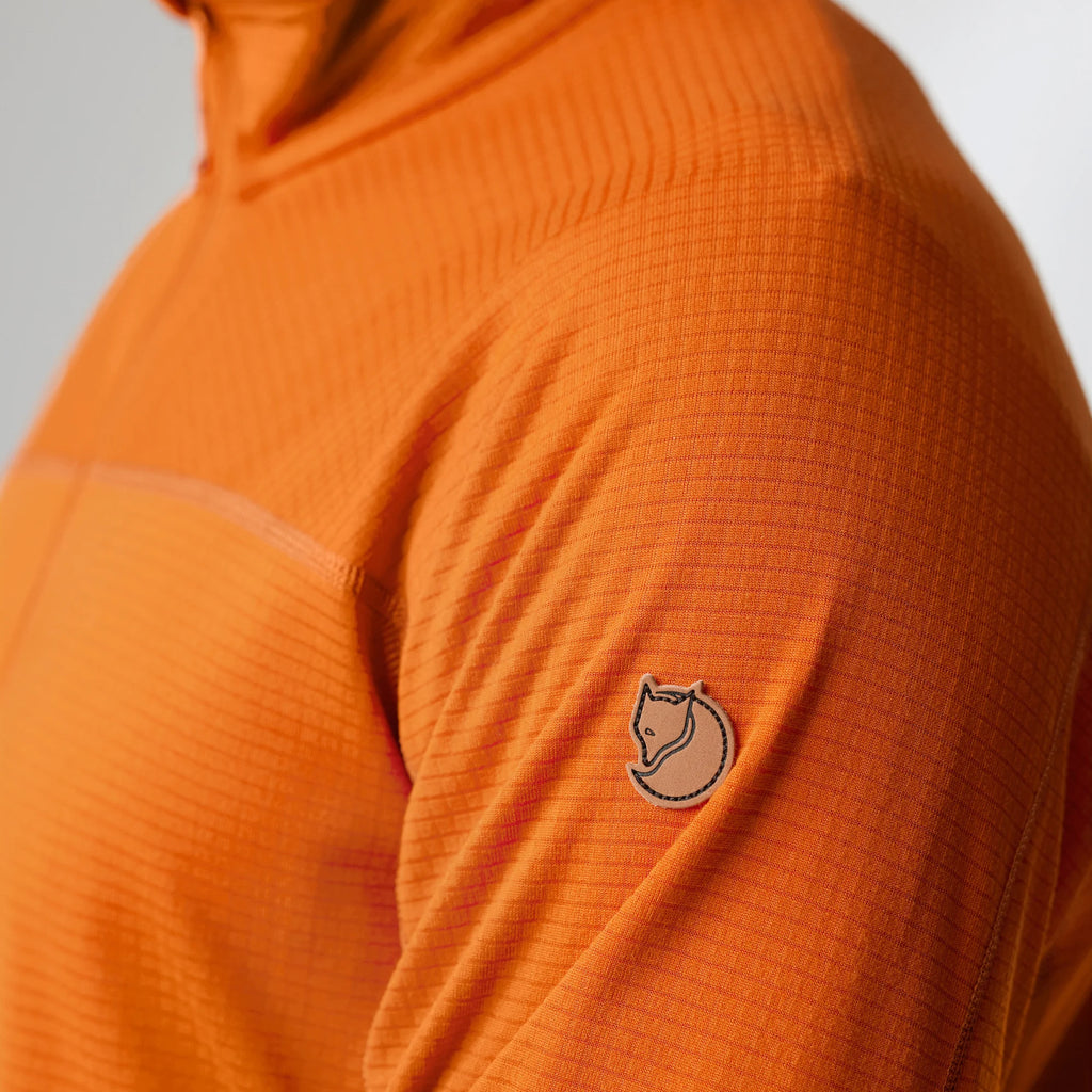 Close-up of an orange textured fleece with a brand logo on the sleeve against a neutral background