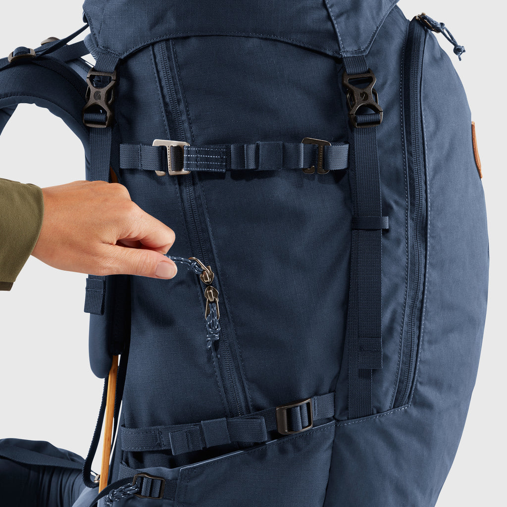Navy blue backpack with a hand adjusting a strap on a light gray background