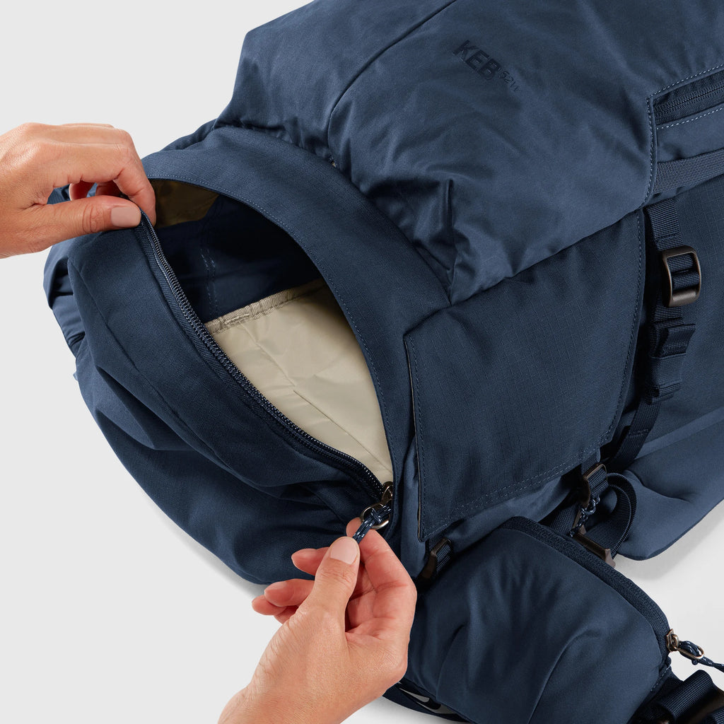 Navy blue backpack with a person opening the zipper on a light gray background