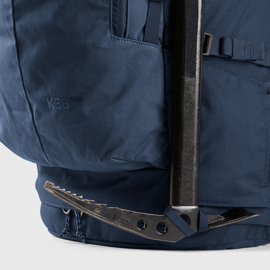 Close-up of a blue backpack with a ice axe attached on a light gray background