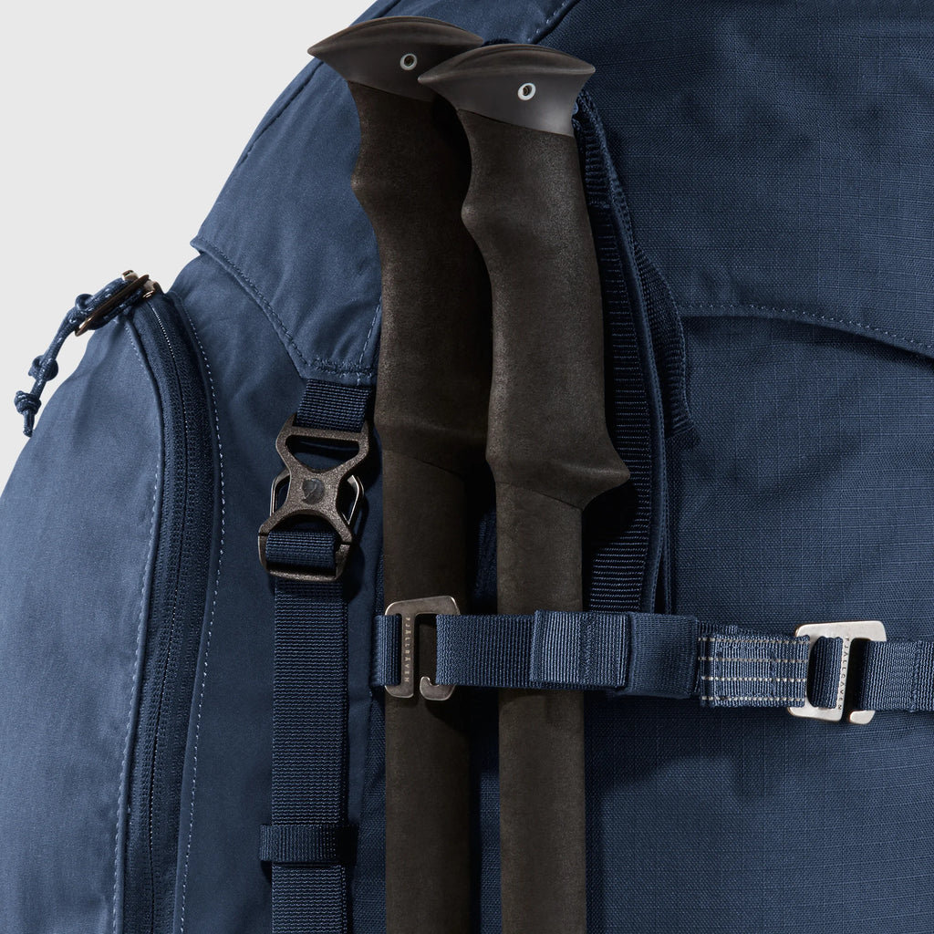 Navy blue backpack with hiking poles attached on a light gray background