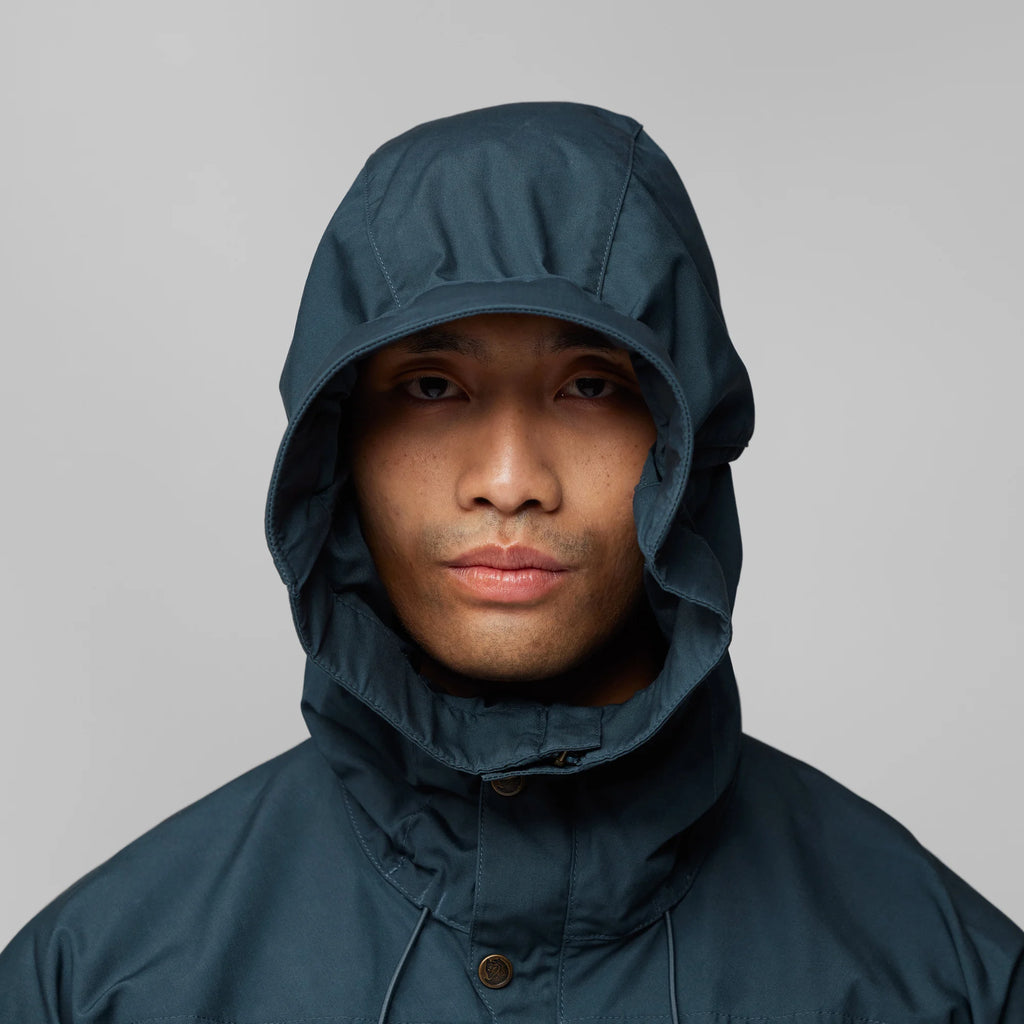 Person wearing a dark blue raincoat with a hood against a gray background