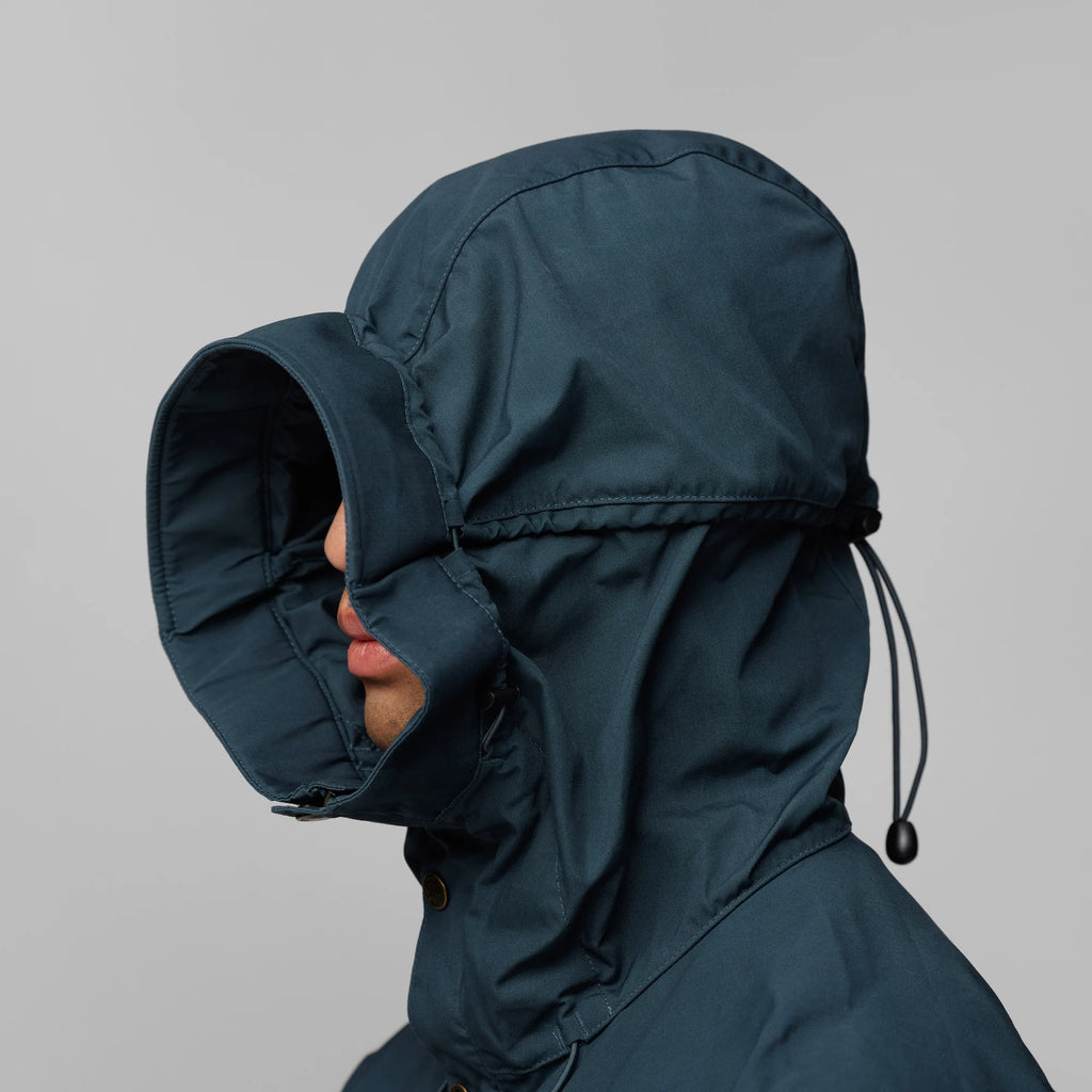 Person wearing a dark blue hooded jacket against a gray background