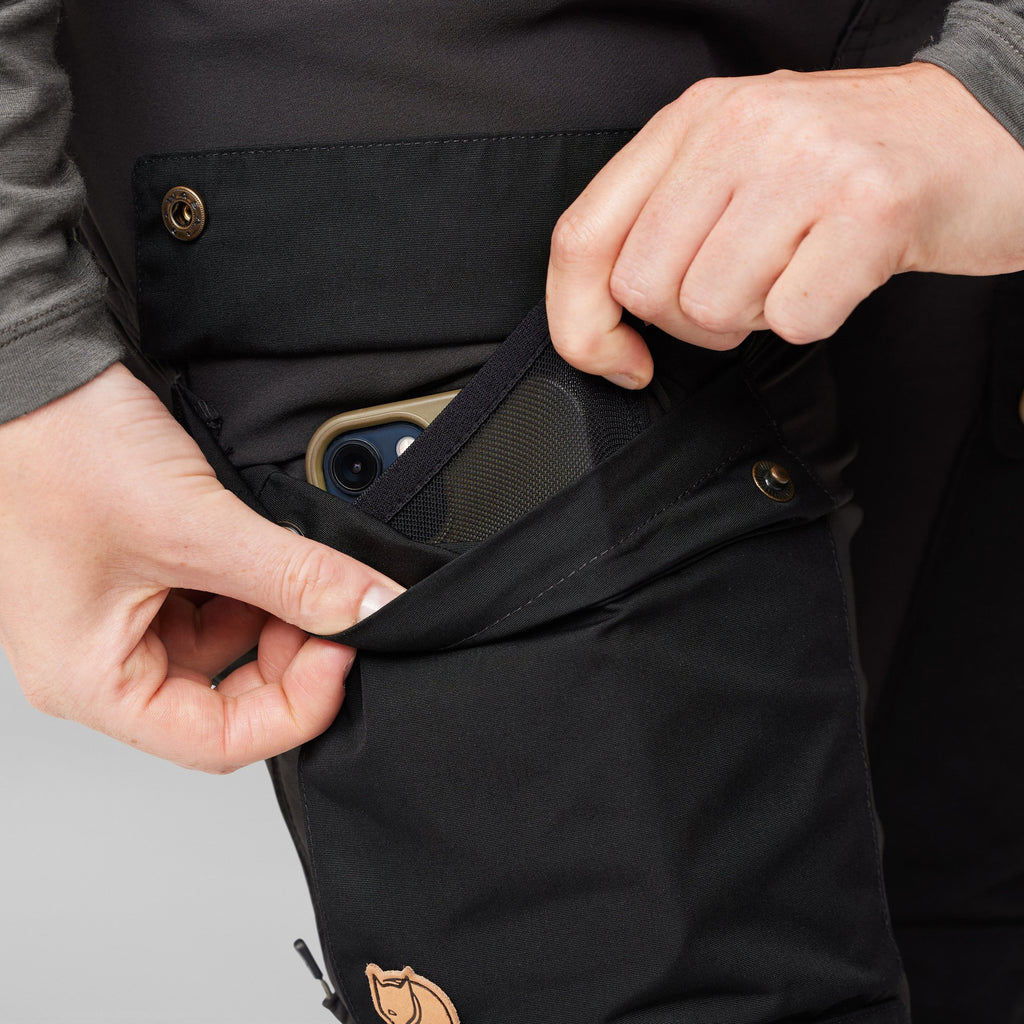 Person putting a phone into a pocket of black pants with a brand logo.