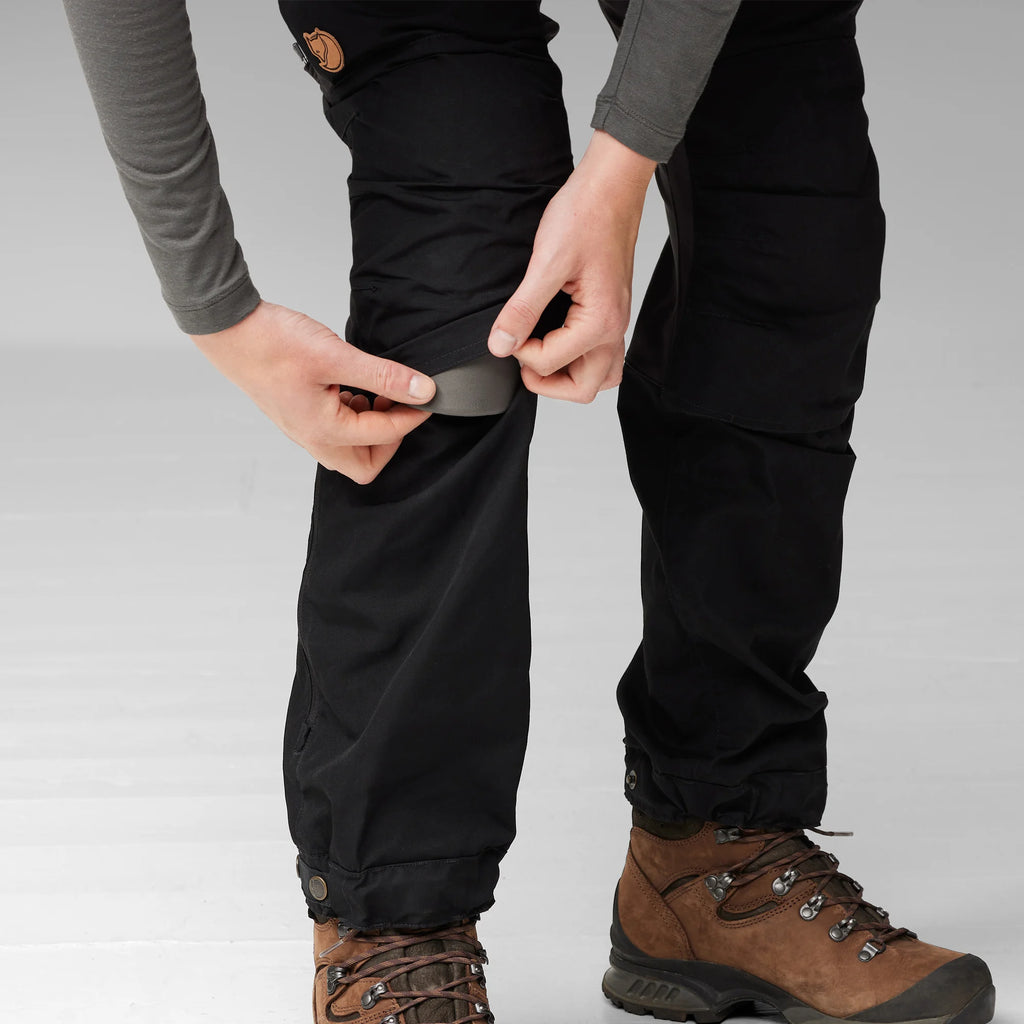 Person wearing black pants and brown boots on a light gray background