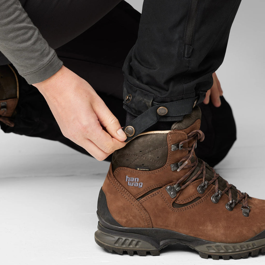 Person adjusting a brown hiking boot with visible brand logo on a light gray background