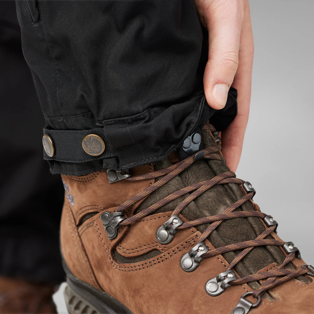 Brown hiking boot with laces being adjusted by a hand against a neutral background