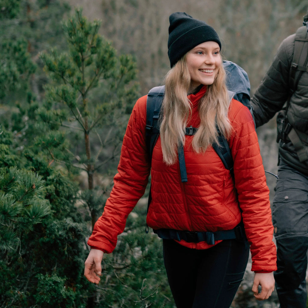 Person wearing a red jacket and black beanie walking through a forest