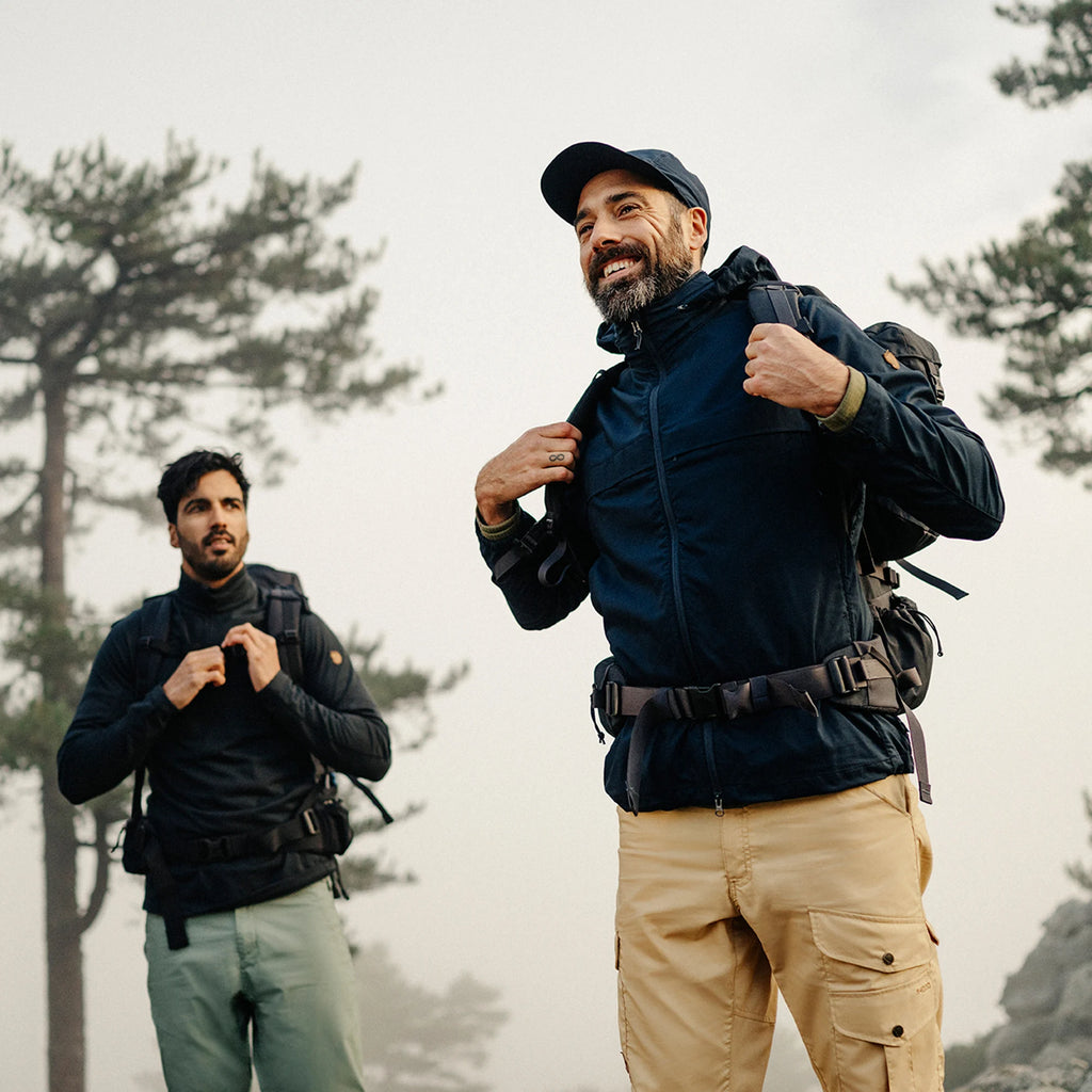 Two men hiking in a forested area, wearing outdoor gear.