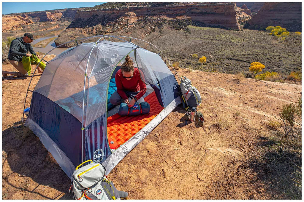 A photo of the Big Agnes Rapide SL Insulated Sleeping Mat within a Big Agnes Tent surrounded by a rocky landscape, and featuring two campers